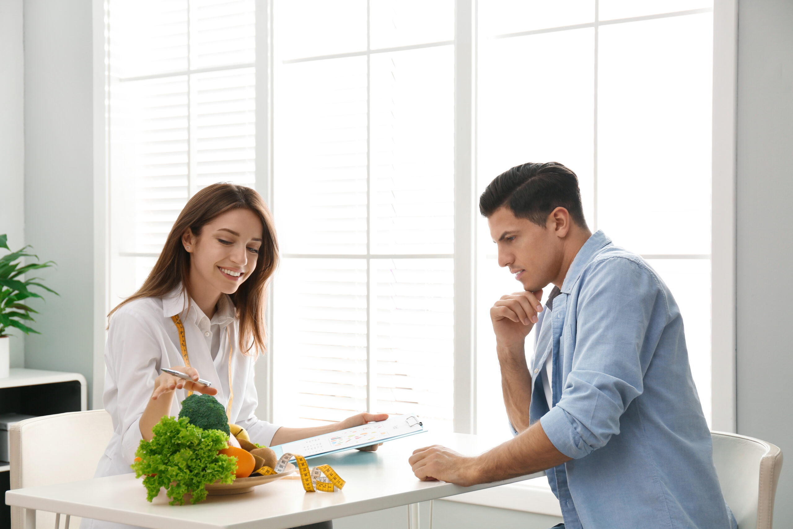 Young Nutritionist Consulting Patient At Table In Clinic
